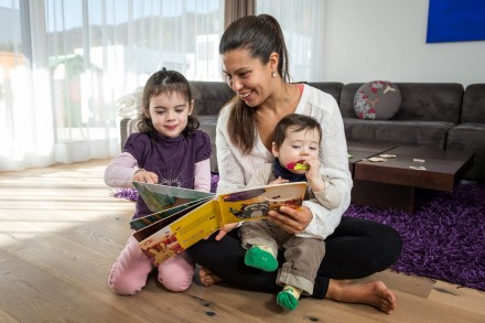 Ein Betreuerin von Kinderbetreuung zu Hause liest zwei Kleinkindern ein Buch vor. 